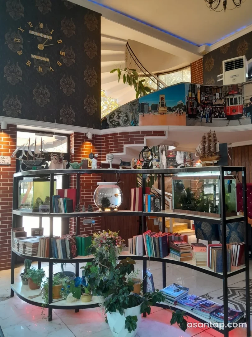 Taksim Corner-də kitab rəfi, gəmi maketləri, məkanın adı yazılmış saat və spiral pilləkən