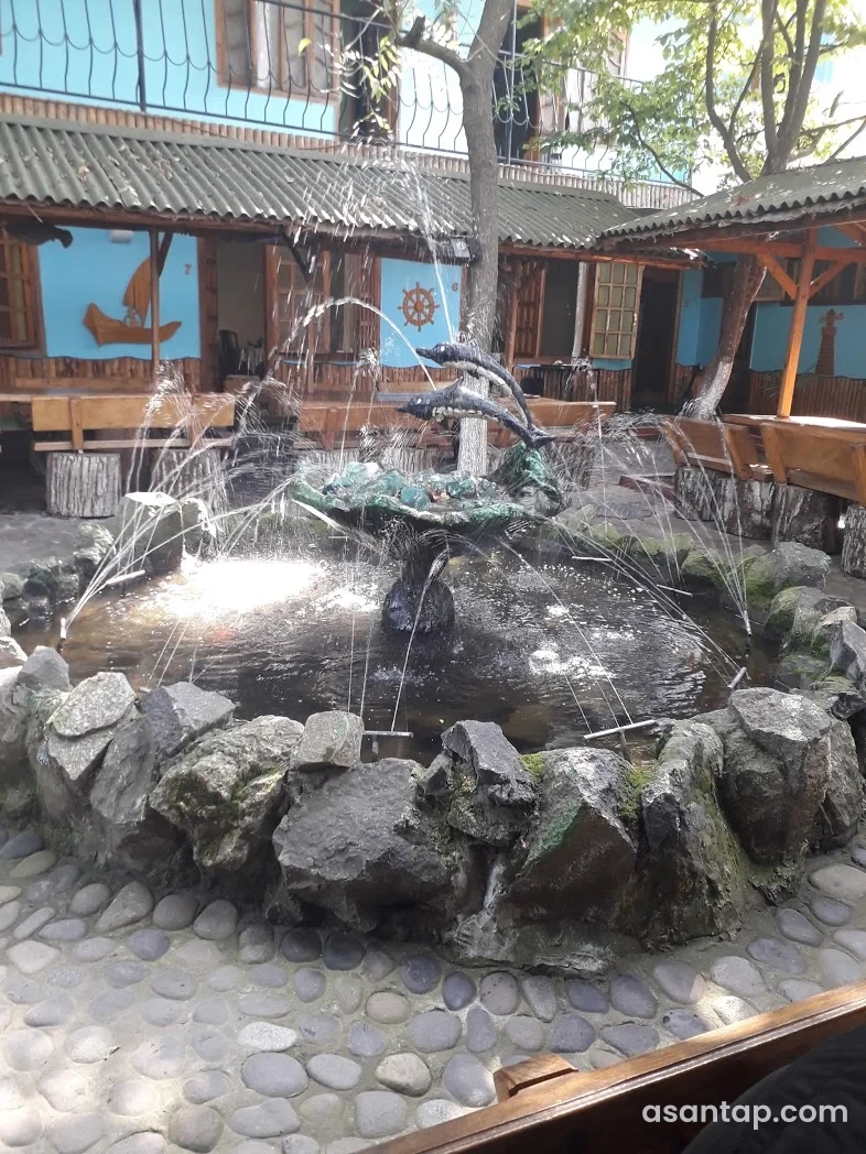 Dalğa restoranının delfin fiqurlu fəvvarəsi, taxta oturacaqları və mavi divarlardakı gəmi dekoru olan həyəti
