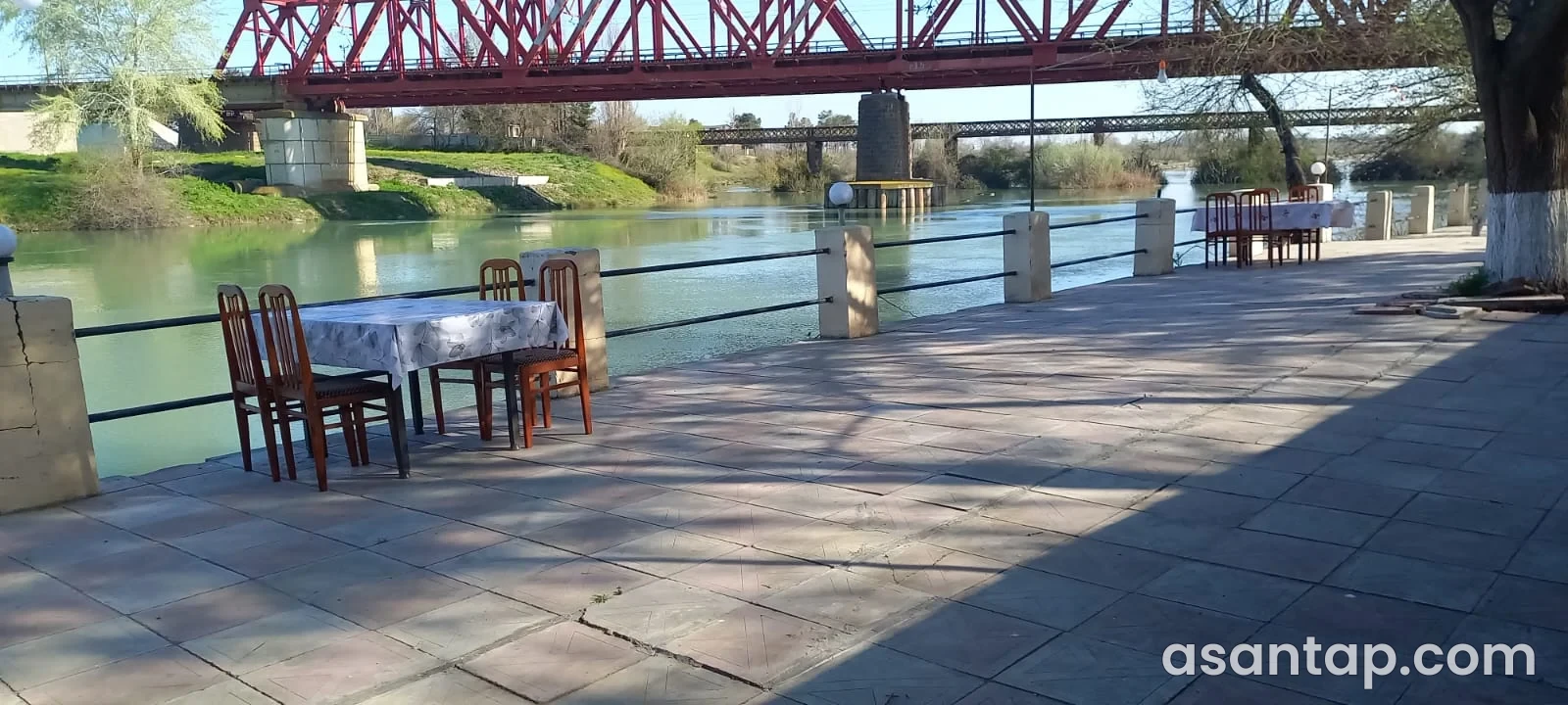 Mayak restoranında Kür çayına və qırmızı metal körpüyə baxan açıq havadakı masalar