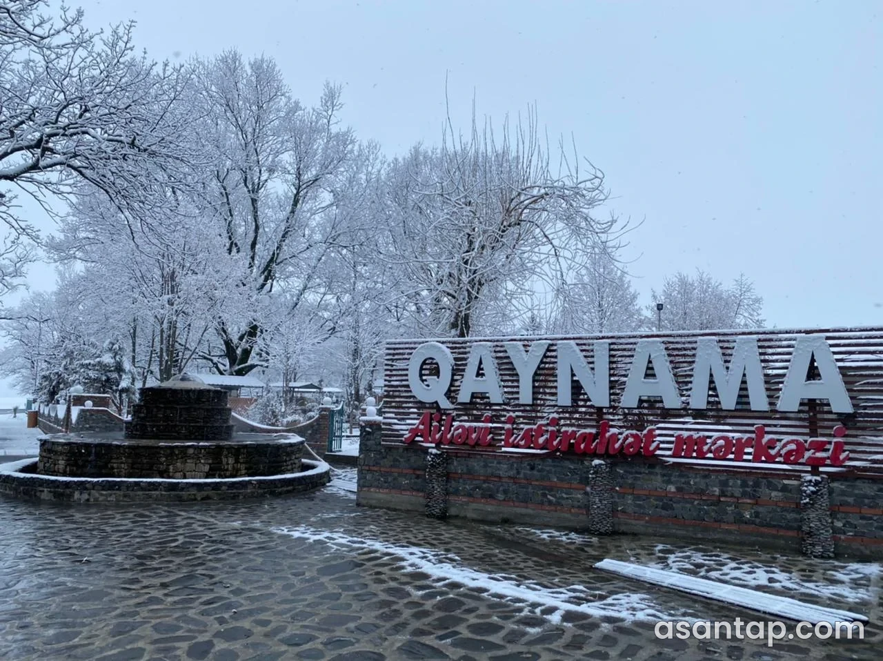 Qaynama Ailəvi İstirahət Mərkəzi yazılı giriş lövhəsi və qarlı həyət