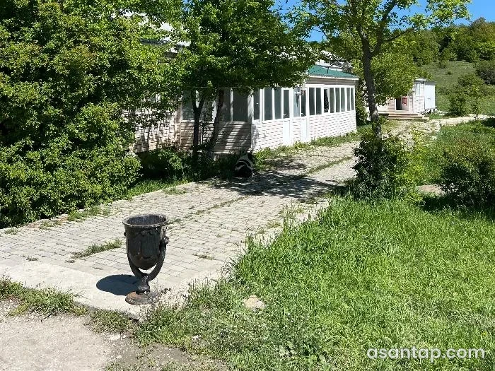 Qızılqazma restoranının ağaclı həyətində şüşəli ağ yemək tikilisi və daş döşənmiş yol
