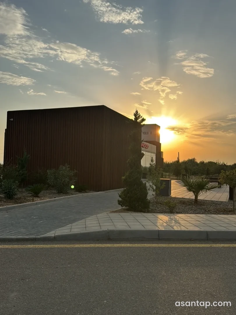 Yevlax Yolüstü restoran-marketinin günbatımında tünd fasadı, lövhəsi və bitkili giriş yolu