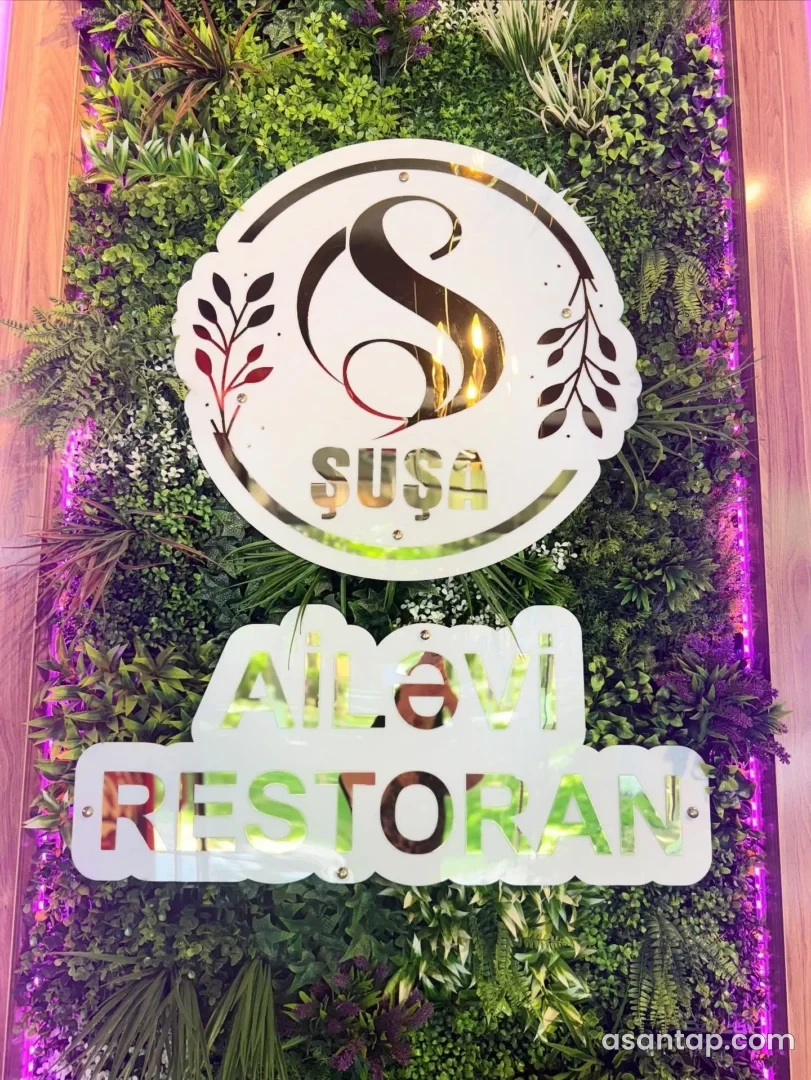 Şuşa Ailəvi Restoranın bitki dekorlu divarındakı işıqlı adı və loqosu