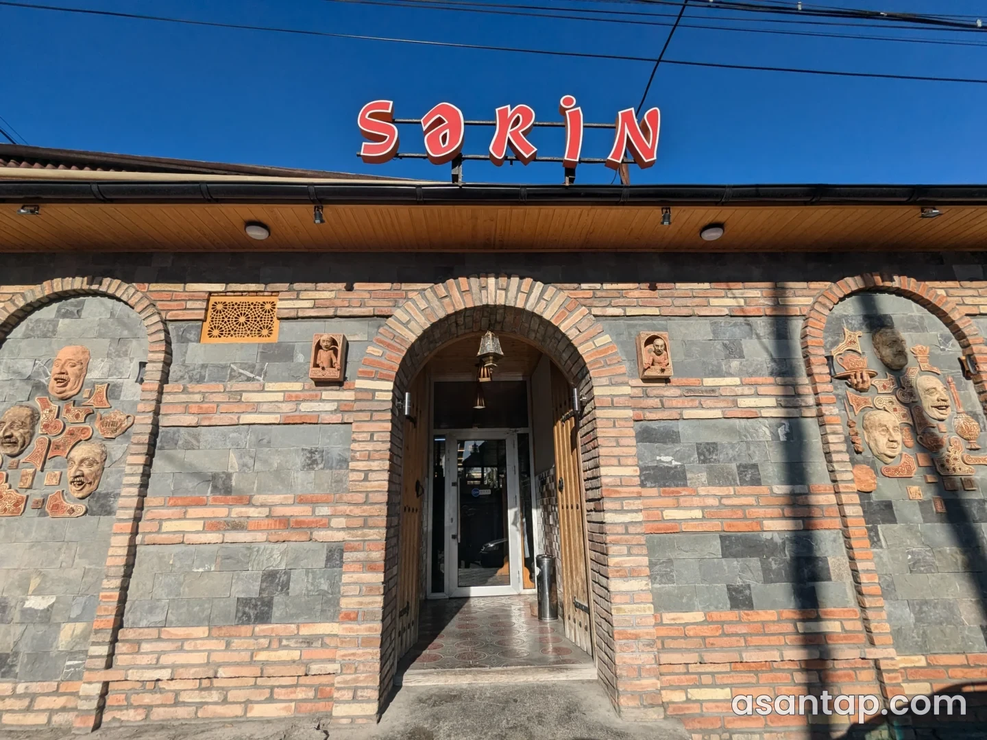 Şəkidə Sərin restoranının qırmızı lövhəli, tağlı daş-kərpic girişi və dekorativ üz təsvirləri