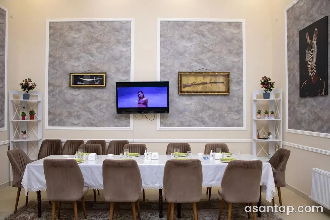 Sahil Restoranında ağ haşiyəli boz divar panelləri, rəflər və uzun süfrə masası olan ayrıca otaq