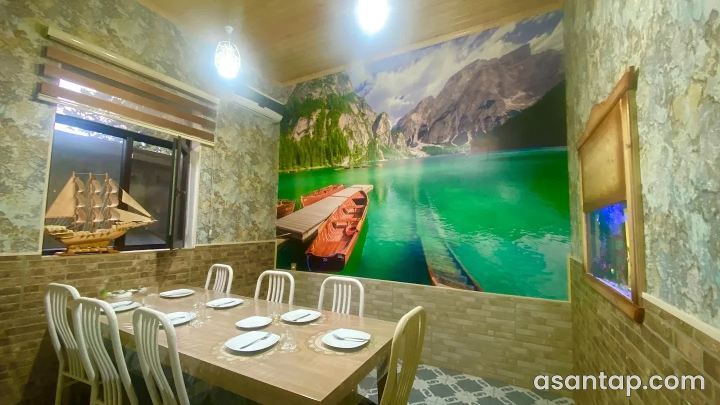 Qazax Məkan restoranının göl mənzərəli divar rəsmi, masa və stulları olan ayrıca yemək otağı