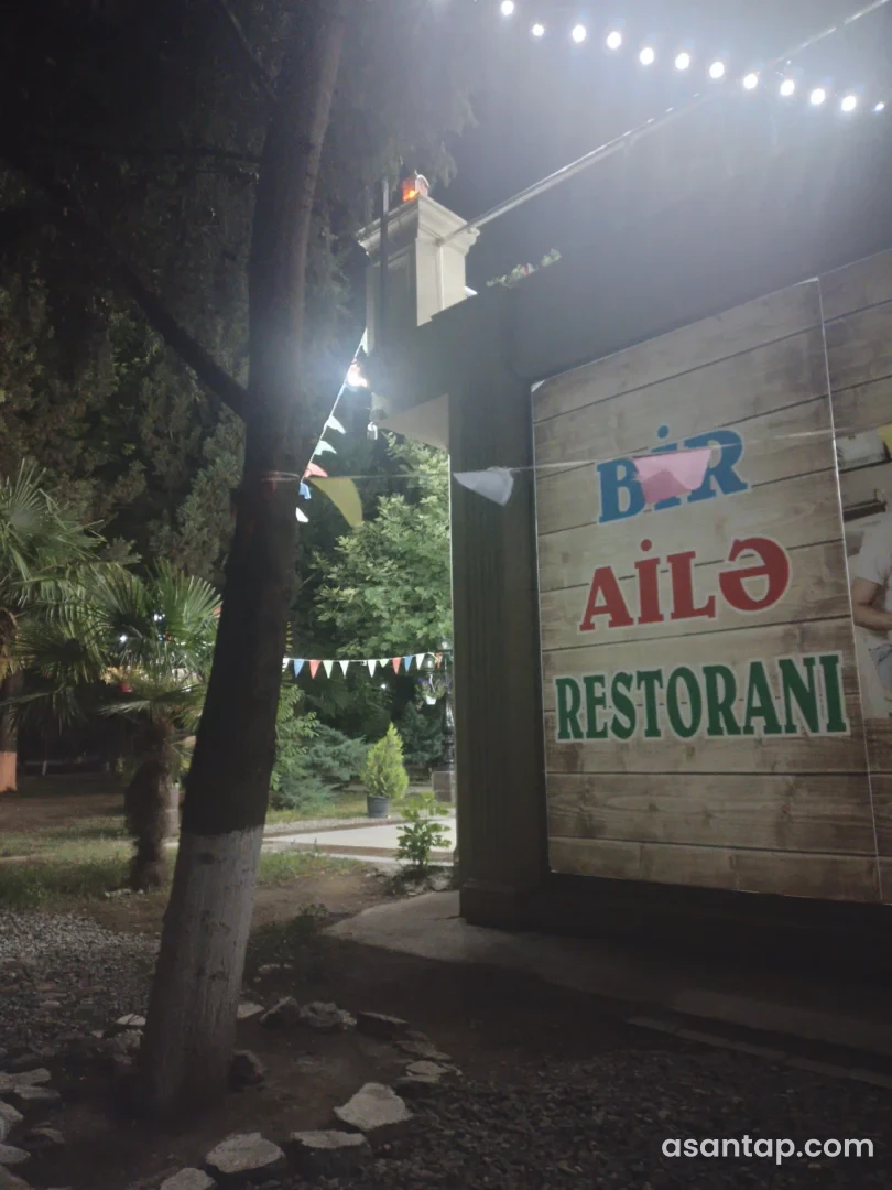Samuxda Bir Ailə Restoranının ad yazılmış taxta giriş hissəsi və ağaclı həyəti