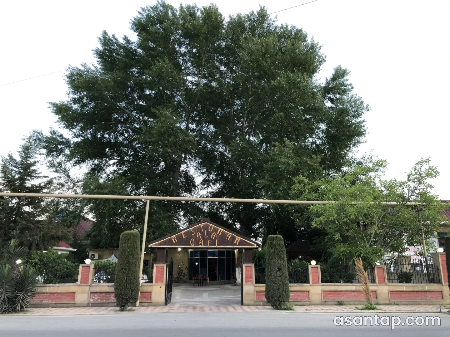 Ağcabədidə Ala Qapı restoranının adı yazılmış ağaclı həyət girişi