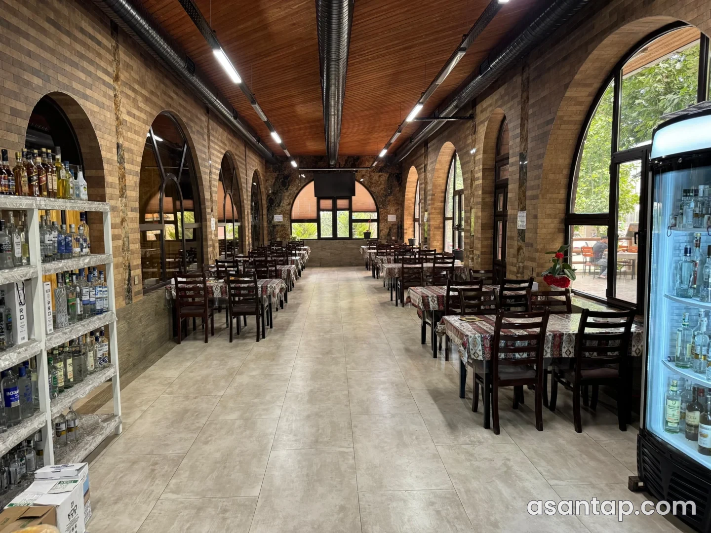 Ləki Restoranın tağlı pəncərəli, taxta tavanlı zalında masalar və tünd ağac oturacaqlar