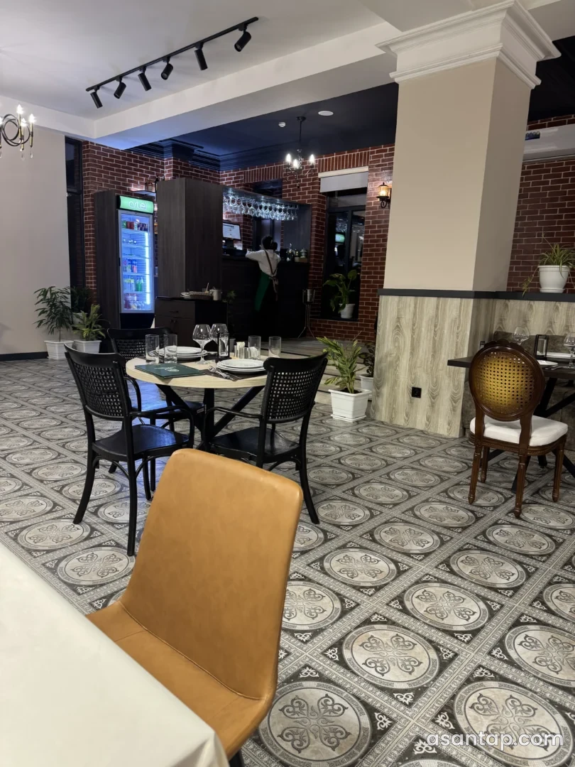 Villa Del Mare restoranının naxışlı döşəməli zalında masalar, qırmızı kərpic dekoru və bar sahəsi