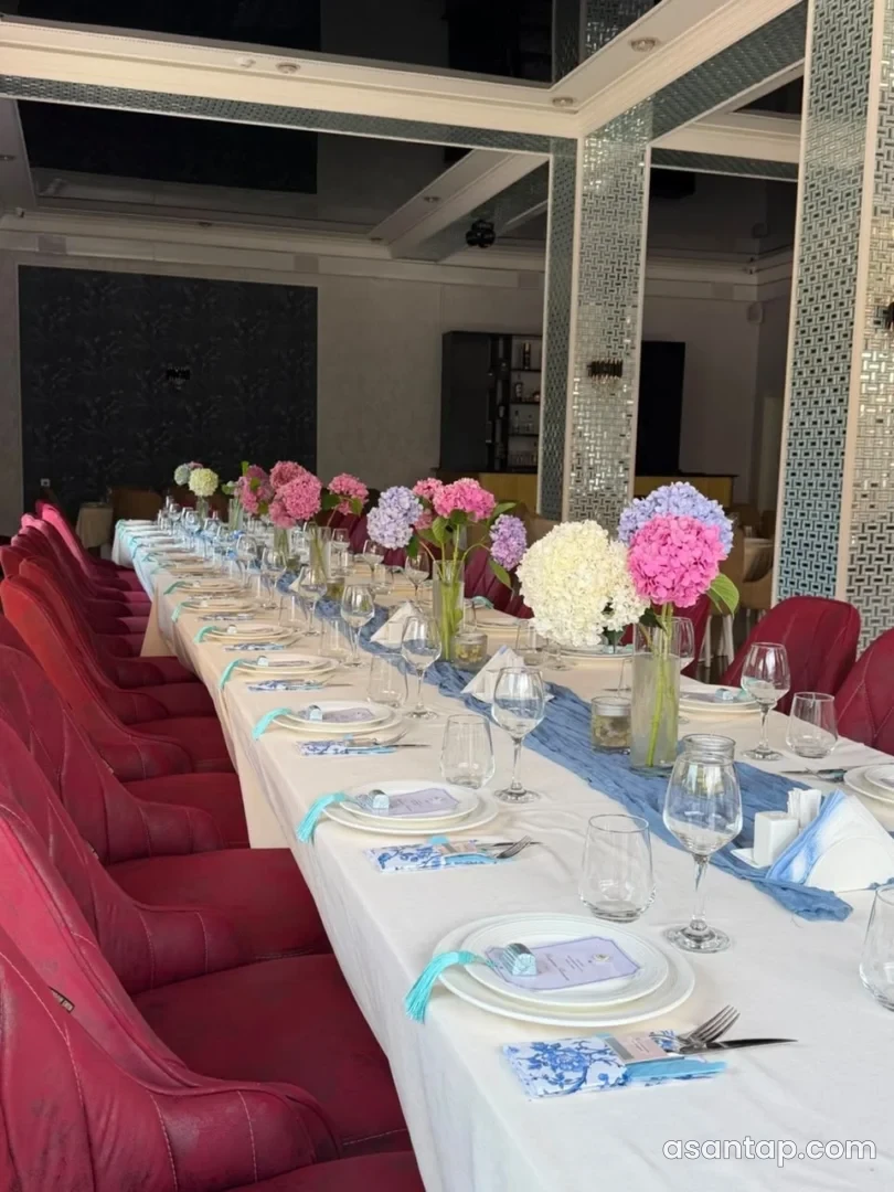 Tenere restoranında güzgülü sütunlar və çiçəklərlə bəzədilmiş uzun yemək masası