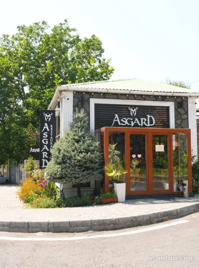 Asgard restoranının yazılı daş fasadı, ağ sütunları və ağac çərçivəli şüşə girişi