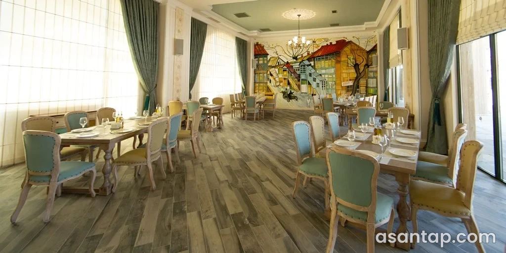 Batumi restoranında rəngli ev rəsmi, yaşıl-krem stullar və iri pəncərəli zal