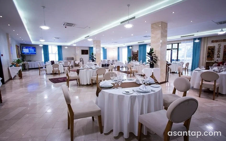 Nuxa restoranının açıq rəngli sütunları, göy pərdələri və ağ örtüklü dairəvi masaları olan salonu