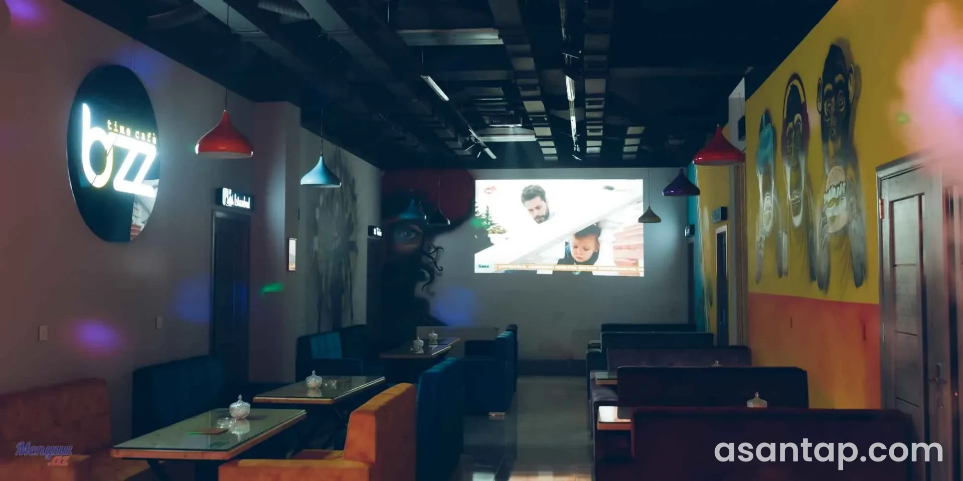Bizz Time Cafe-nin işıqlı loqosu, rəngli asma lampaları, divanlı masaları və böyük ekranı olan zalı