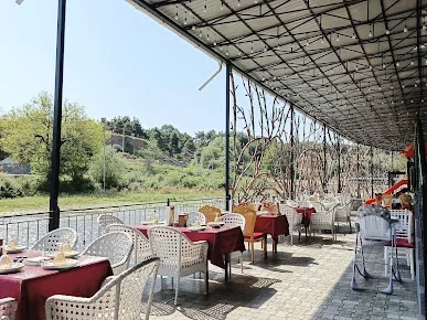 Atmosfer restoranında çay kənarında üstüörtülü teras, qırmızı örtüklü masalar və ağ hörmə stullar