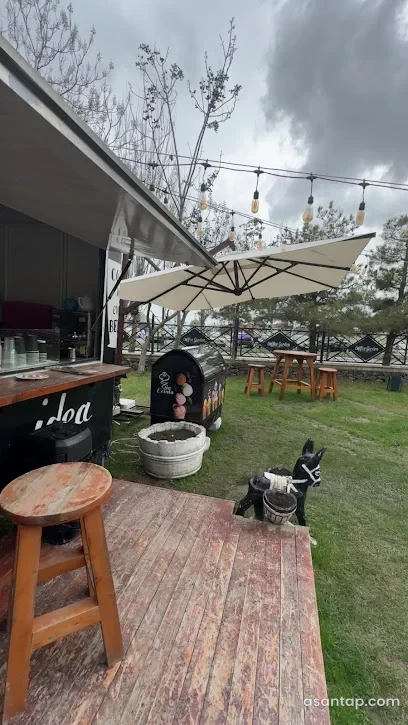 Coffee Garden-də açıq qəhvə sayğacı, taxta oturacaqlar, çətirlər və yaşıllıq