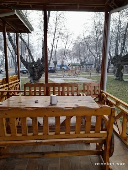 Qızılağac restoranında ağaclı həyətə baxan taxta masalı və skamyalı örtülü pavilyon