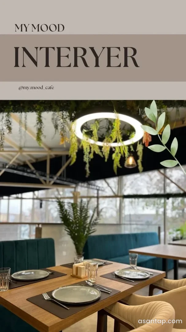 My Mood Cafe-nin iri pəncərəli salonunda yaşıl divanlar, bej kreslolar və qurulmuş masalar