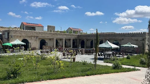 Kəhriz Restoranın tağlı daş fasadı qarşısında masa və çətirləri olan yaşıllıqlı açıq həyət