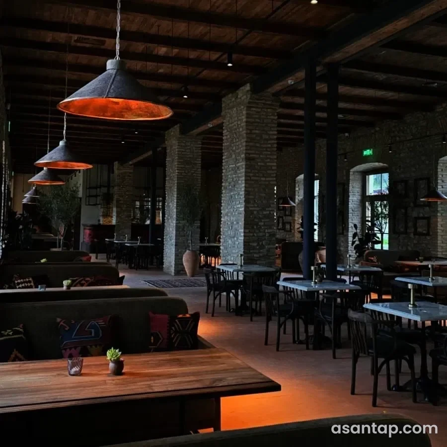 Kilim Şəki restoranının kərpic sütunlu, taxta tavanlı və misrəngli asma işıqlı yemək salonu