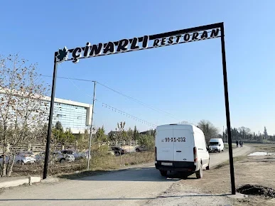 Sabirabadda Çinarlı Restoranın yarpaq nişanlı qara giriş lövhəsi və ağaclı həyətə aparan yol