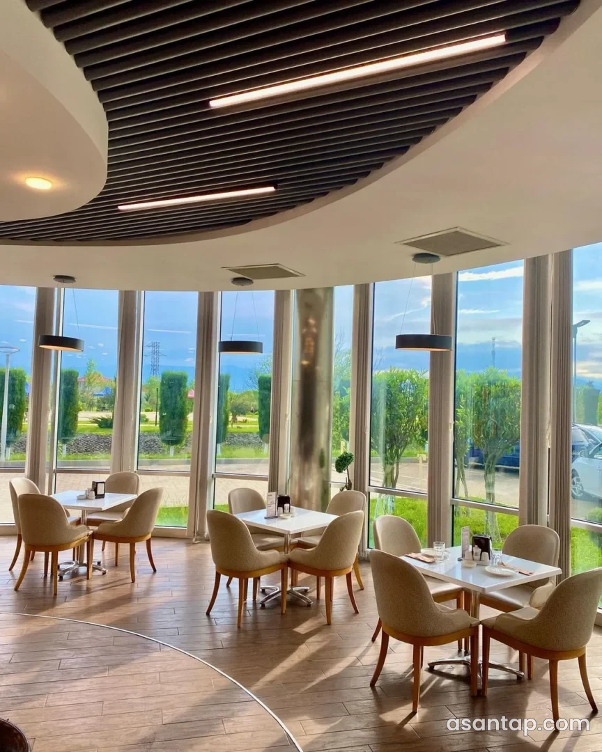 Kafe O-nun panoramik şüşəli, bej kreslolu və ağ masalı salonu