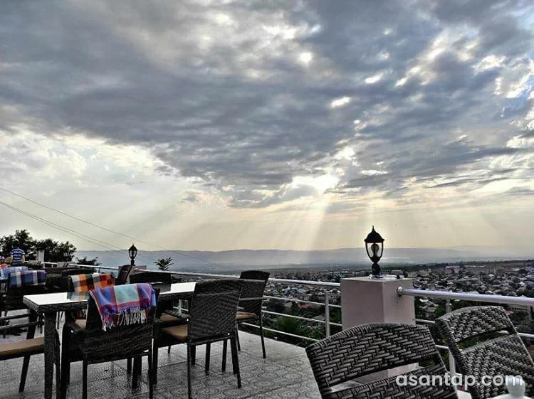 Qala restoranının Şəki şəhərinə baxan metal məhəccərli açıq terrası, hörmə kreslolar və masalar