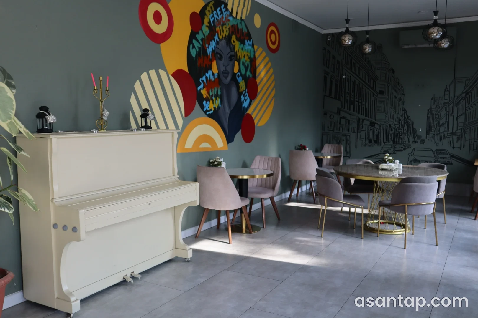 Route62 salonunda ağ piano, rəngli qadın və şəhər xətti divar rəsmləri, dairəvi masalar