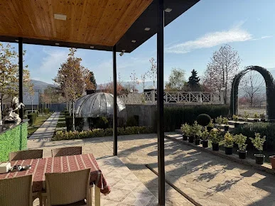 Sevimli Bağın şüşəli terrasından görünən şəffaf günbəzli oturma hissəsi, ağ hasar və bağ yolu