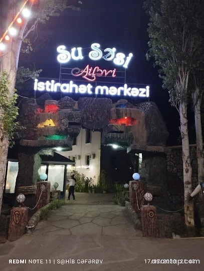 Su Səsi ailəvi istirahət mərkəzinin işıqlı yazısı, daş görünüşlü tağlı girişi və ağaclı həyəti