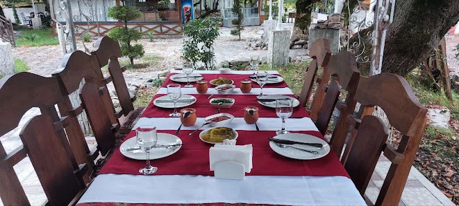 Elvin restoranının bağında ağac altında qırmızı-ağ süfrəli masa, taxta stullar və arxada pavilyon