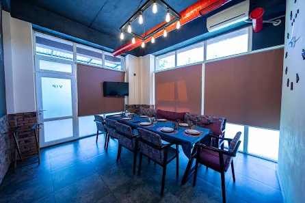 VIP House Qəbələ restopubunda geniş pəncərəli ayrıca oturma sahəsi, süfrə açılmış masa və rəngli yumşaq oturacaqlar