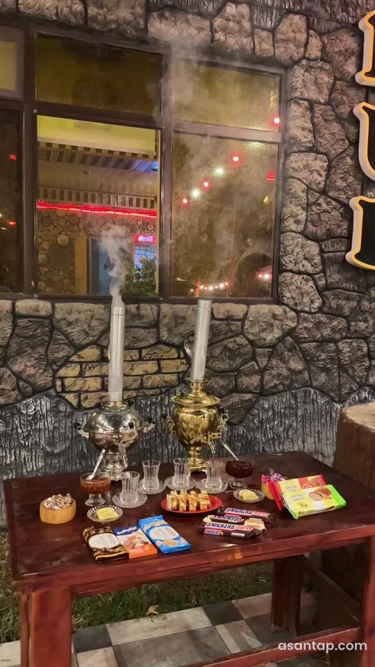 Ağdərə Pub-da daş görünüşlü divar qarşısında buxarlanan samovarlarla çay süfrəsi