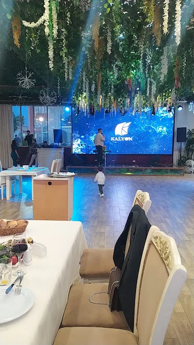 Kalyon restoranında səhnə, Kalyon yazılı ekran, sallanan yaşıllıq dekoru və yemək masaları