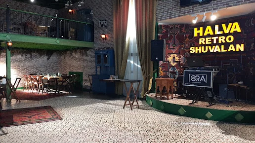 Halva Şüvəlanın retro zalında adlı lövhə, xalçalı səhnə və masalar