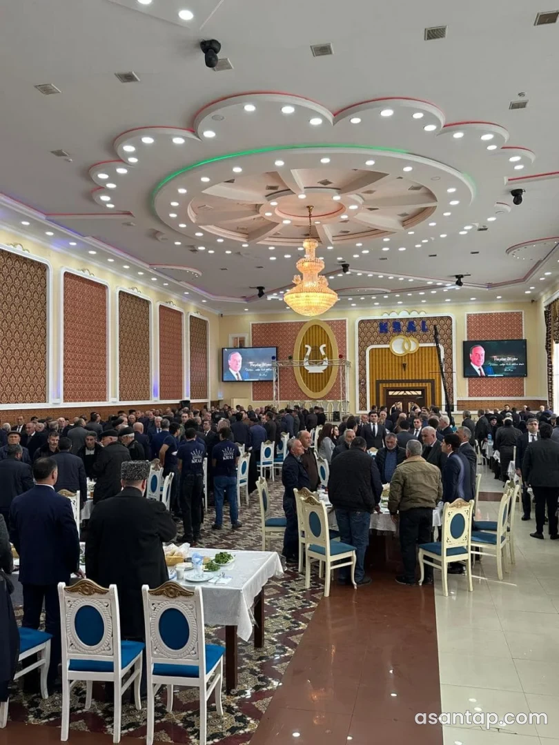 Kral şadlıq sarayının KRAL yazılı dekorativ divarı, çilçıraqları və məclis masaları görünən banket zalı