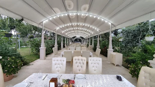 Dörd Fəsil restoranının ağ örtüklü bağ oturma sahəsində masalar, açıq rəngli stullar və yaşıllıqlar