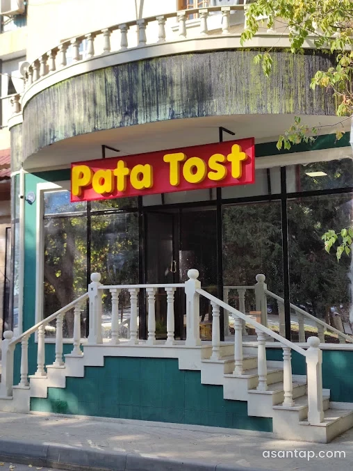Mingəçevirdə Pata Tost məkanının sarı-qırmızı lövhəli şüşə girişi və ağ məhəccərli pilləkənləri