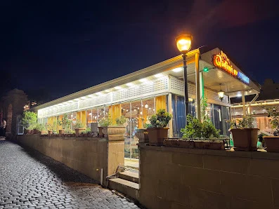 Qədimi Ev restoranının şüşələnmiş zalı, güldanlarla bəzədilmiş giriş pilləkənləri və işıqlı fasadı
